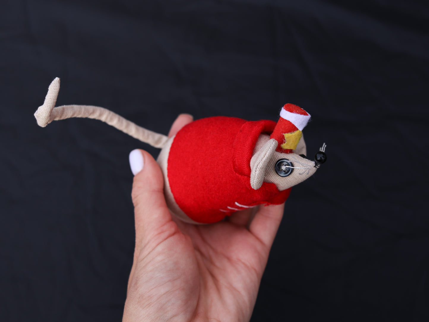 Hand holding a toy mouse dressed in a red outfit against a dark background