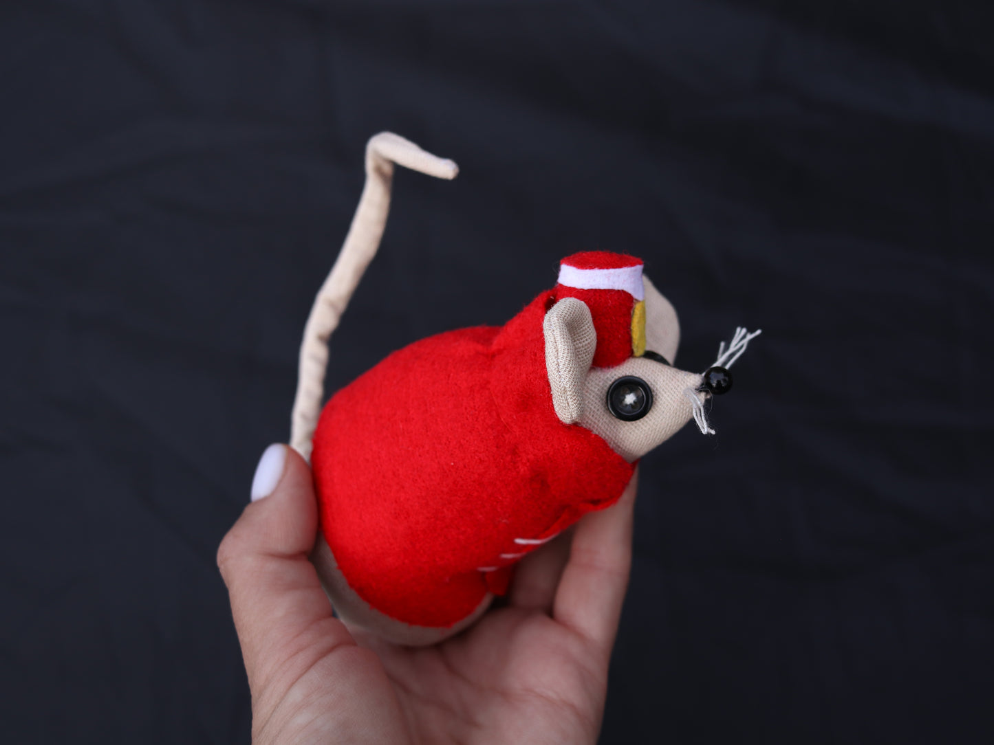Red plush toy mouse held in a hand against a dark background
