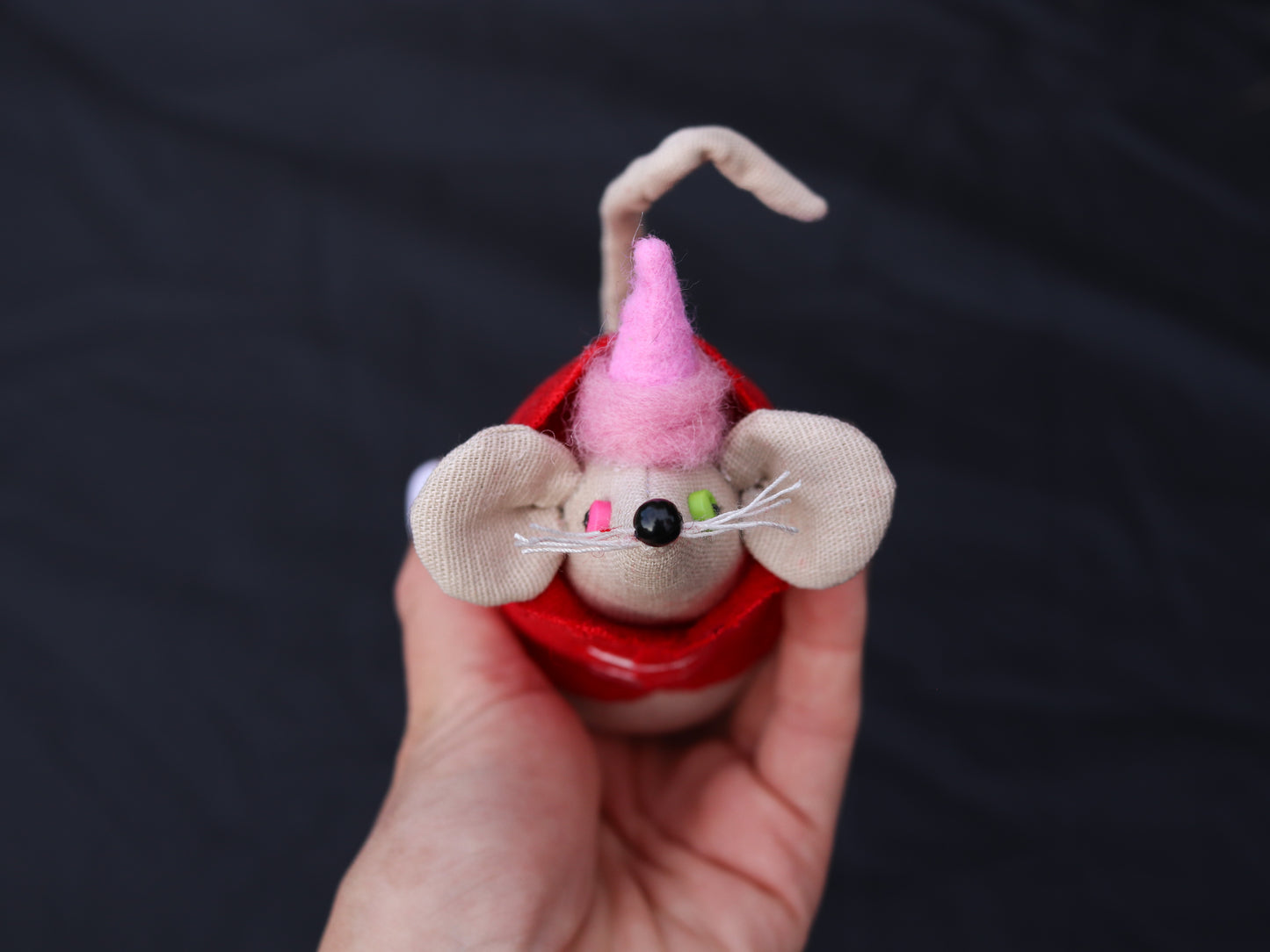Hand holding a small toy mouse with a pink hat against a dark background
