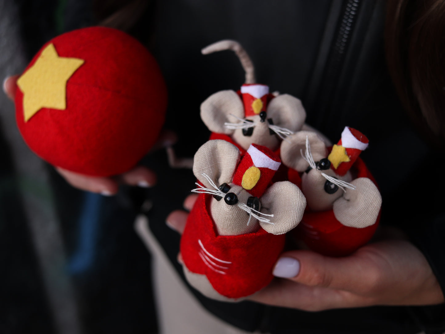 Three small plush mice toys in red outfits held by a person against a dark background.