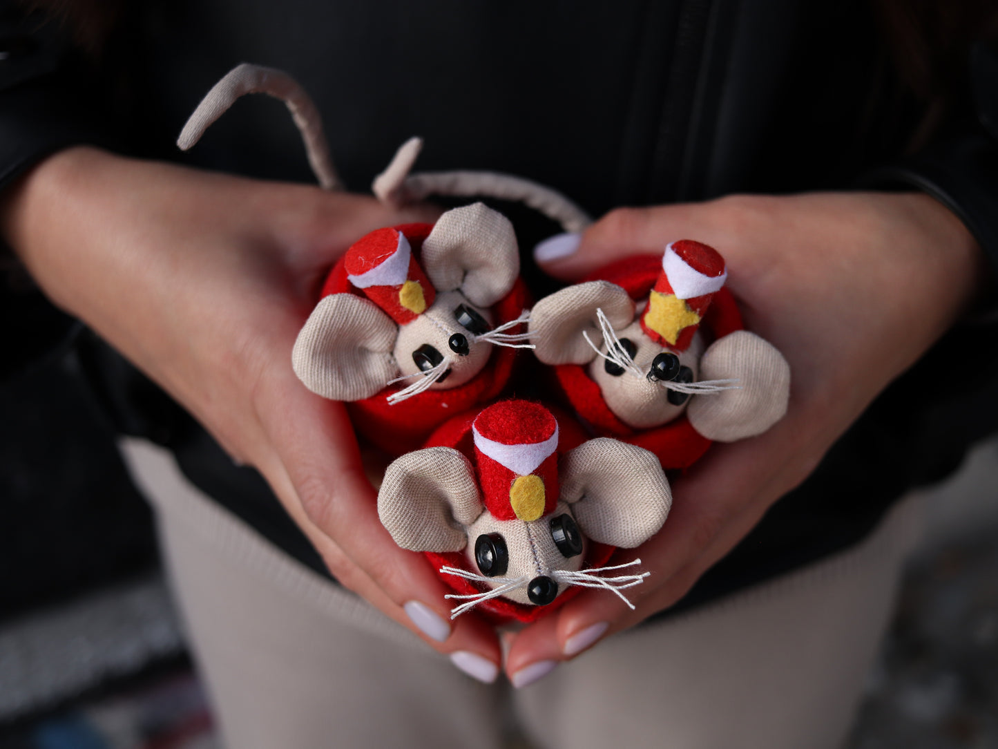 Three small toy mice dressed in circus hats held in hands against a dark background
