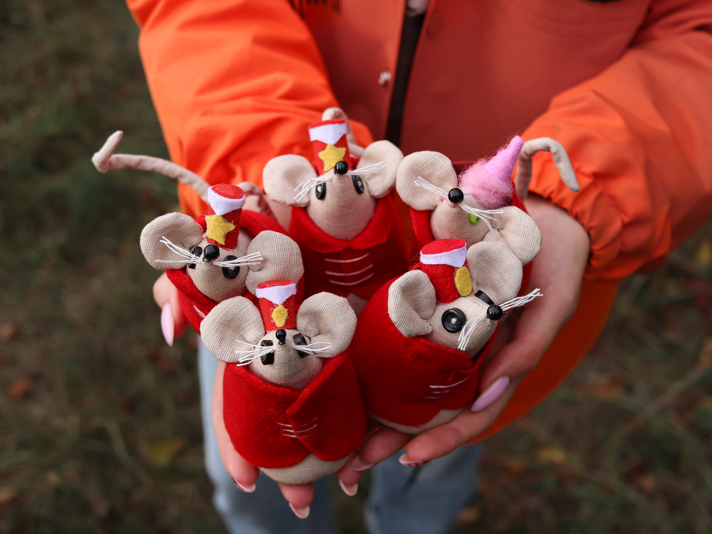 Person holding small stuffed toy mice dressed in circus outfits against a blurred natural background