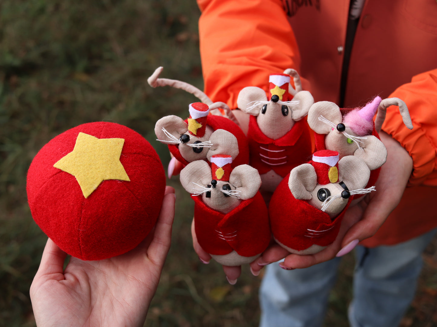 Red plush mice with circus hats held by a person in an orange jacket.