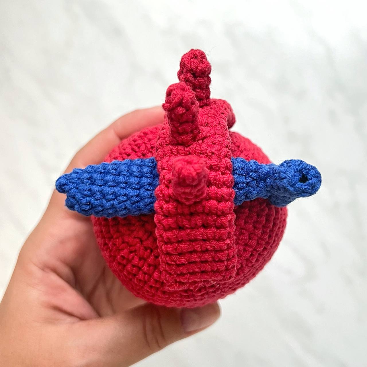 Hand holding a red and blue crocheted heart-shaped object against a white background
