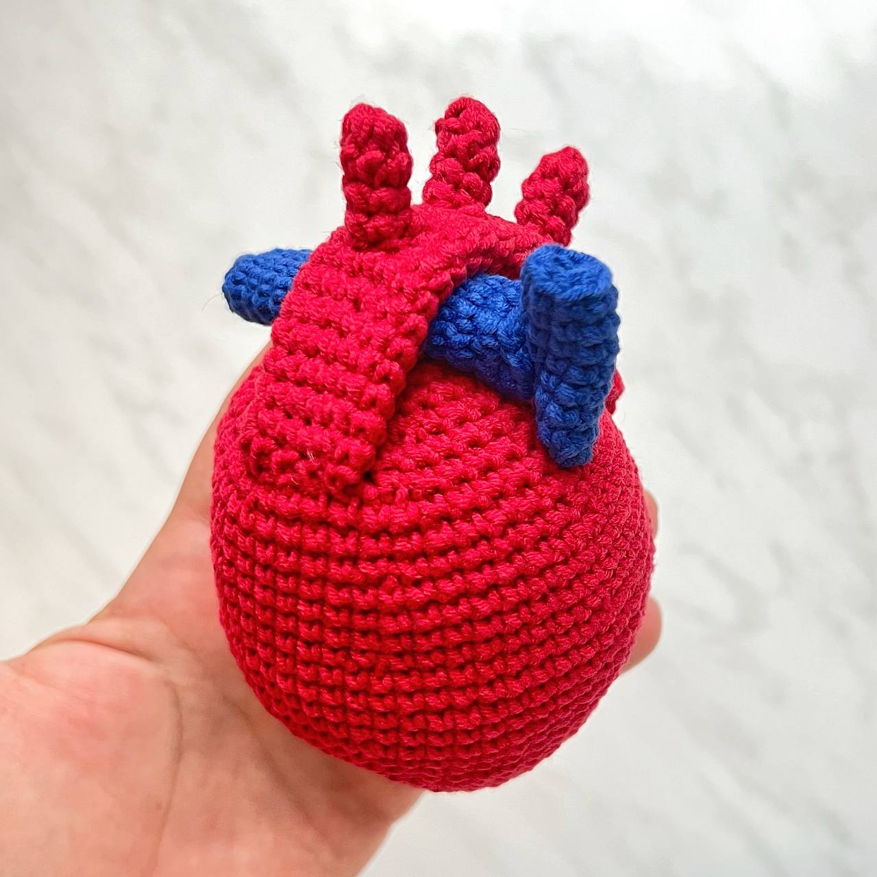 Handmade crochet heart with blue wings held in a hand against a white background