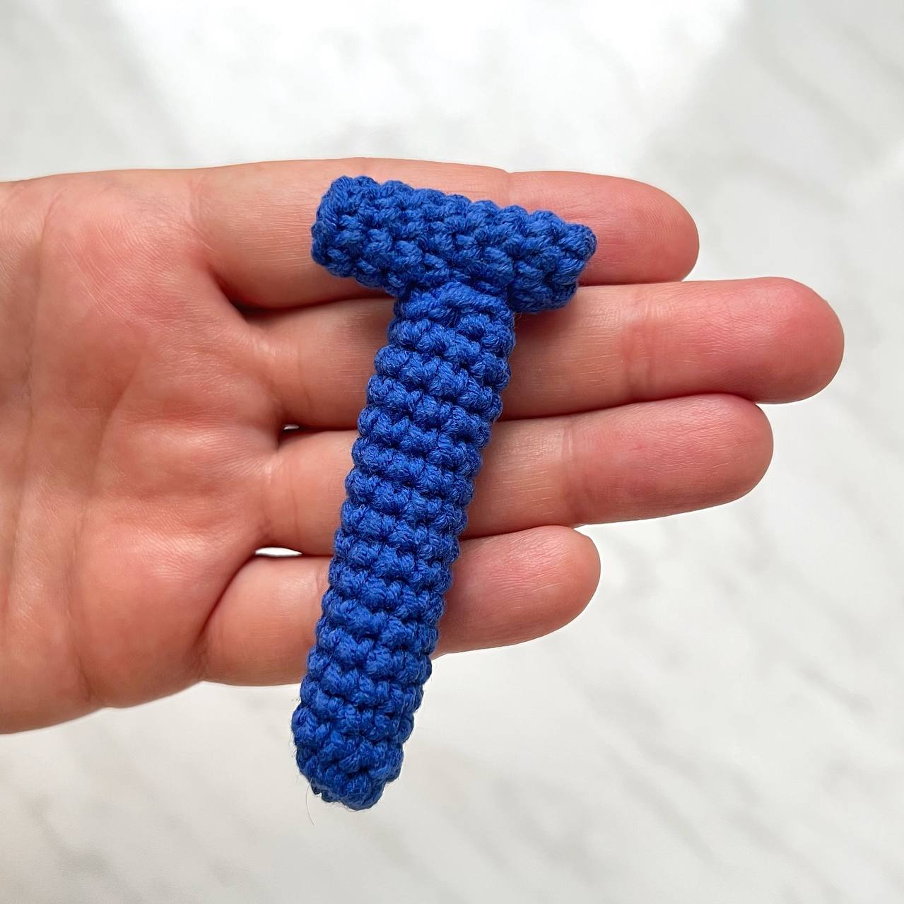 Blue knitted element held in a hand against a white background