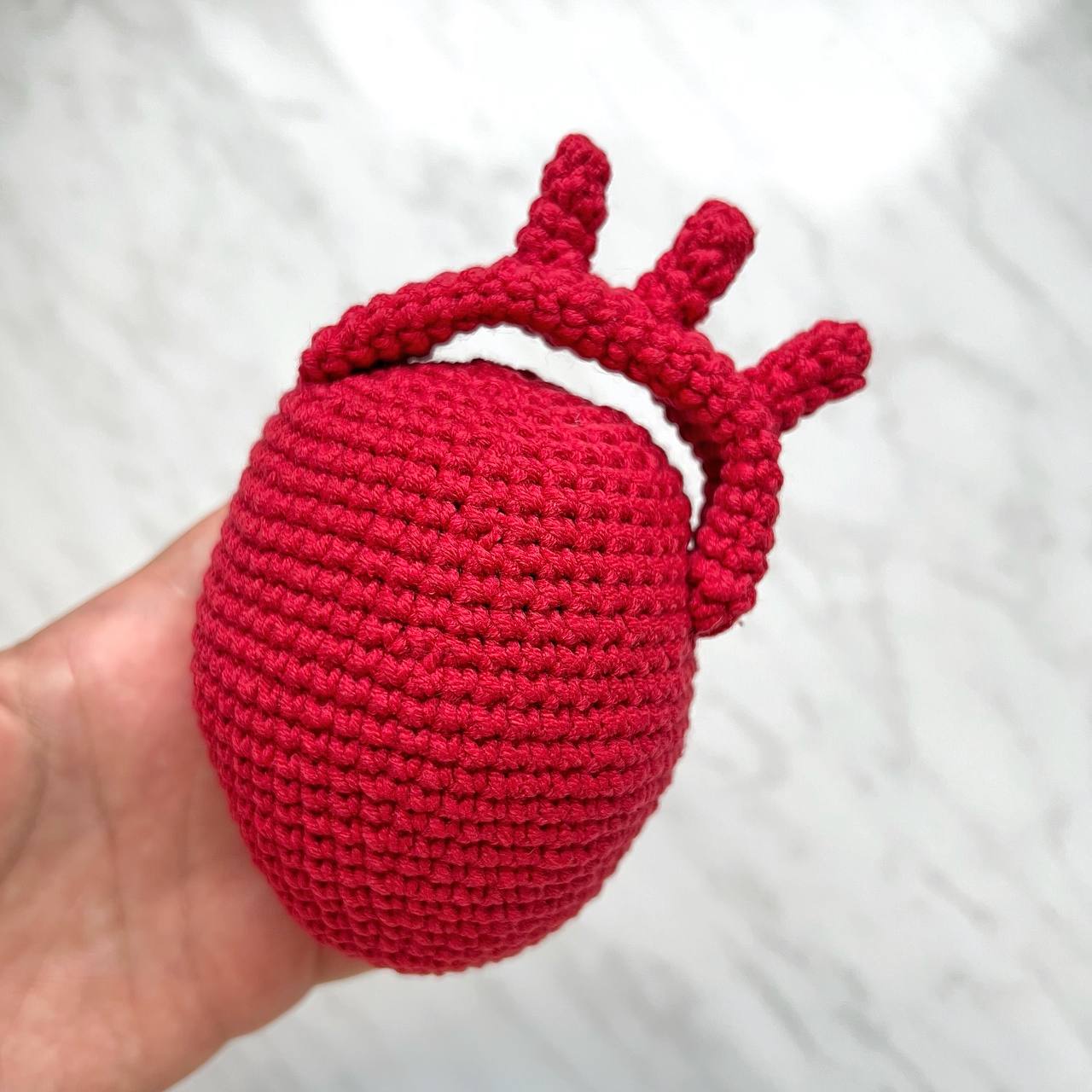 Red crochet heart held in a hand against a white background