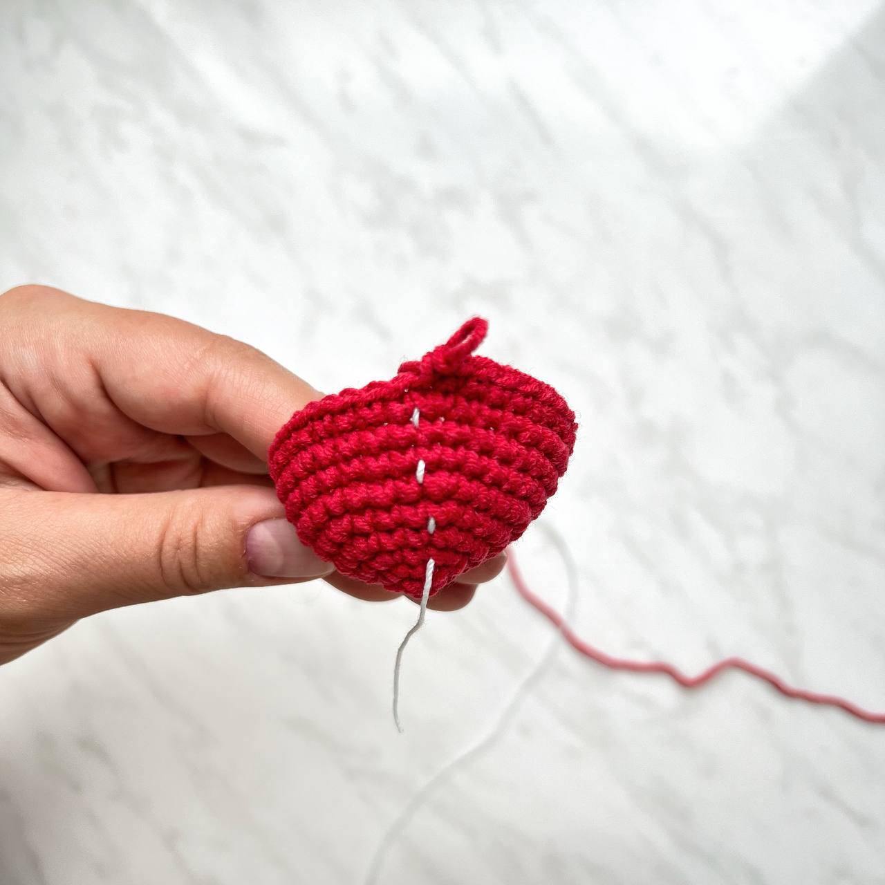 Hand holding a red crochet project with a needle on a white background