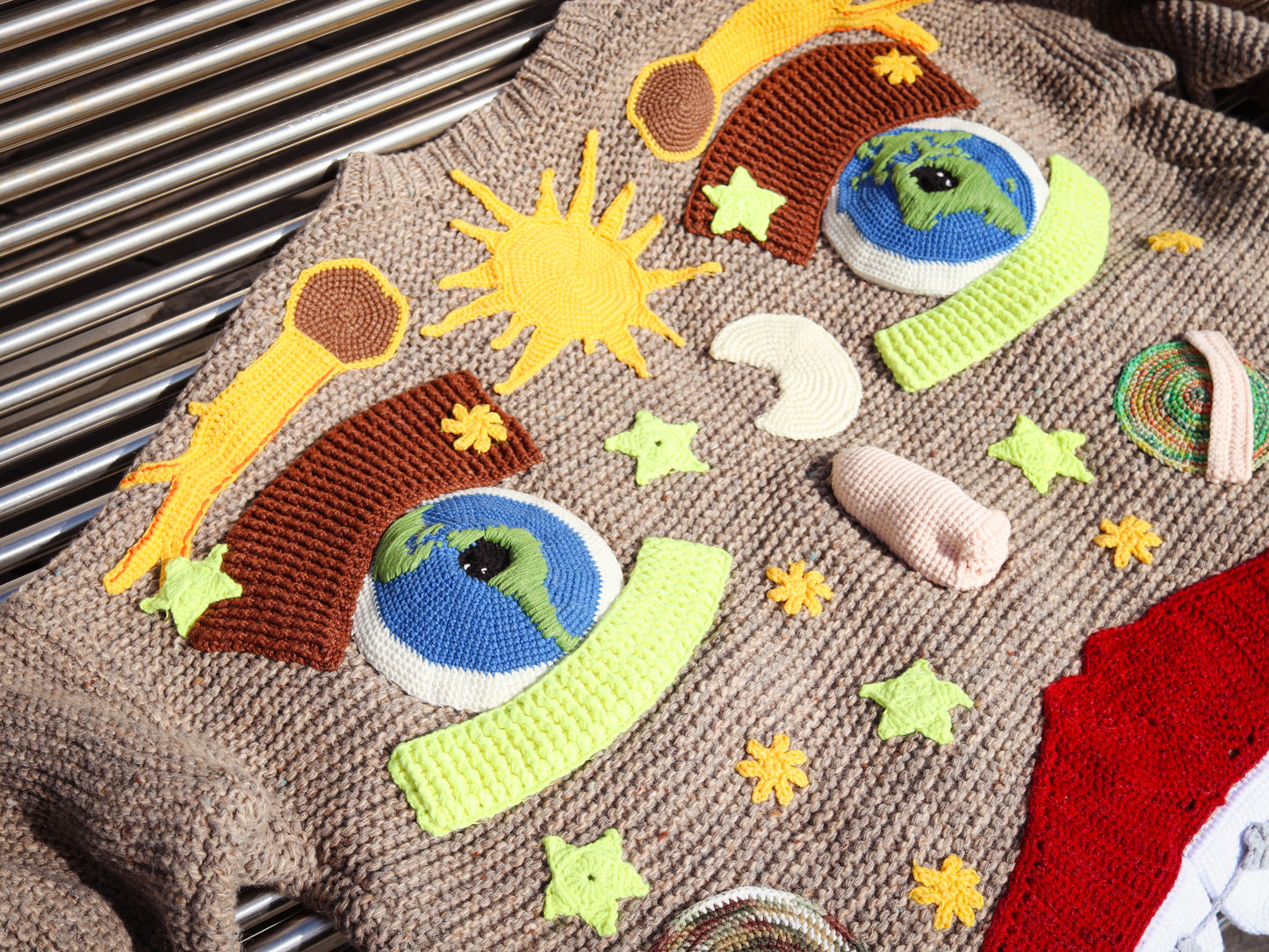 Knitted sweater with colorful space-themed appliqués on a metal surface.