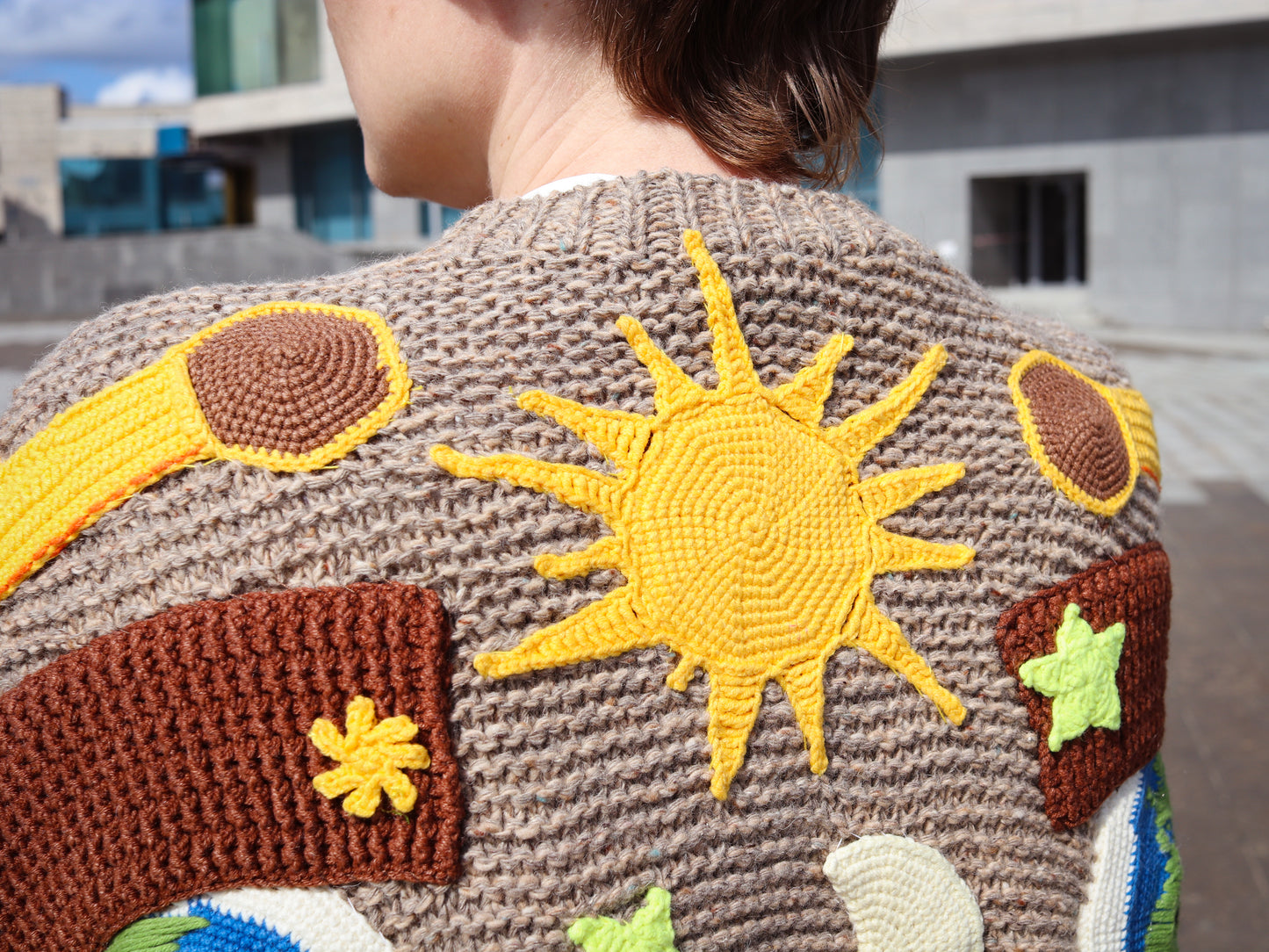 Person wearing a brown knitted sweater with colorful sun and cloud patterns.