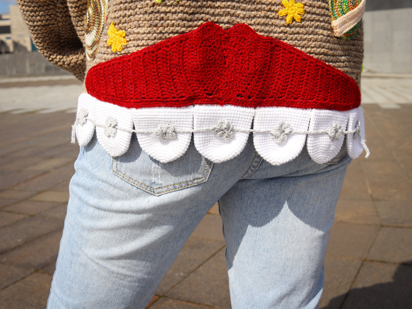 Person wearing a sweater with a red and white design and light blue jeans.