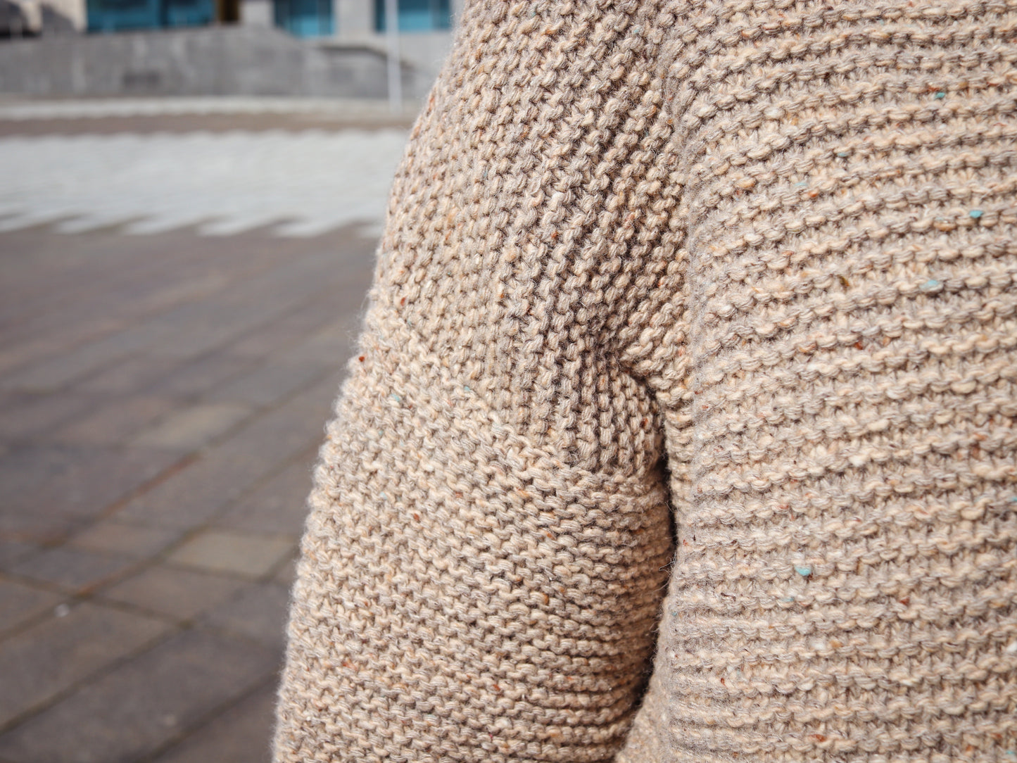 Close-up of a textured beige sweater sleeve with a blurred outdoor background