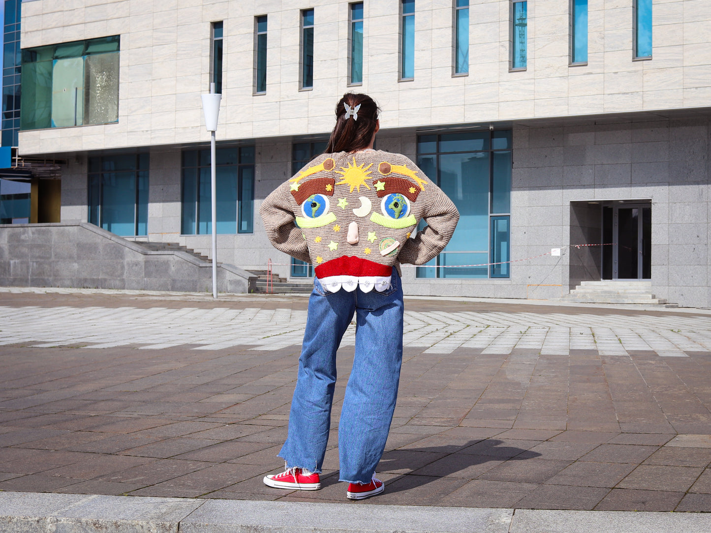 Person wearing a colorful knit cardigan with a cartoon design in front of a building.