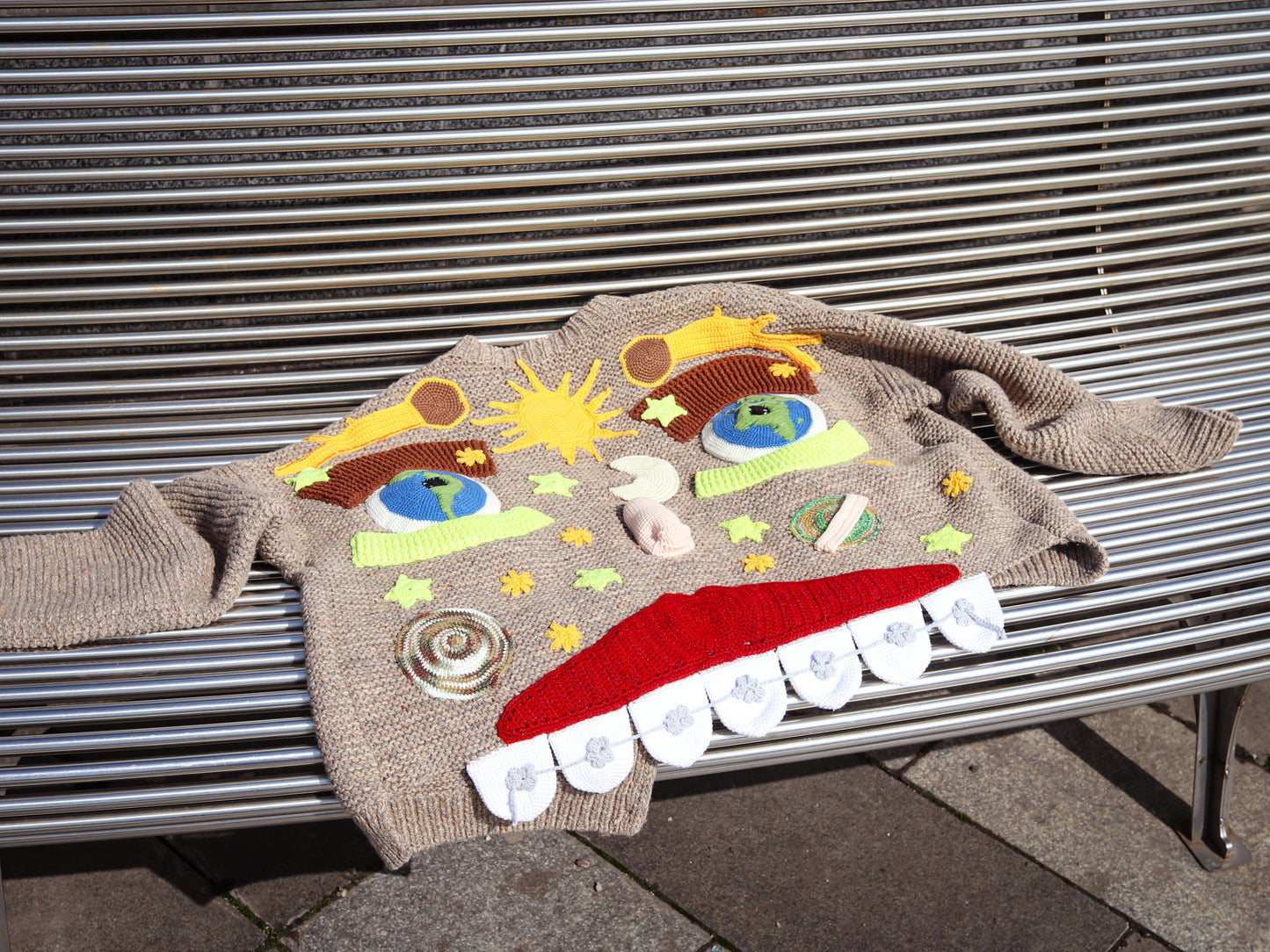 Colorful hooded cardigan with cartoon face design on a metal bench