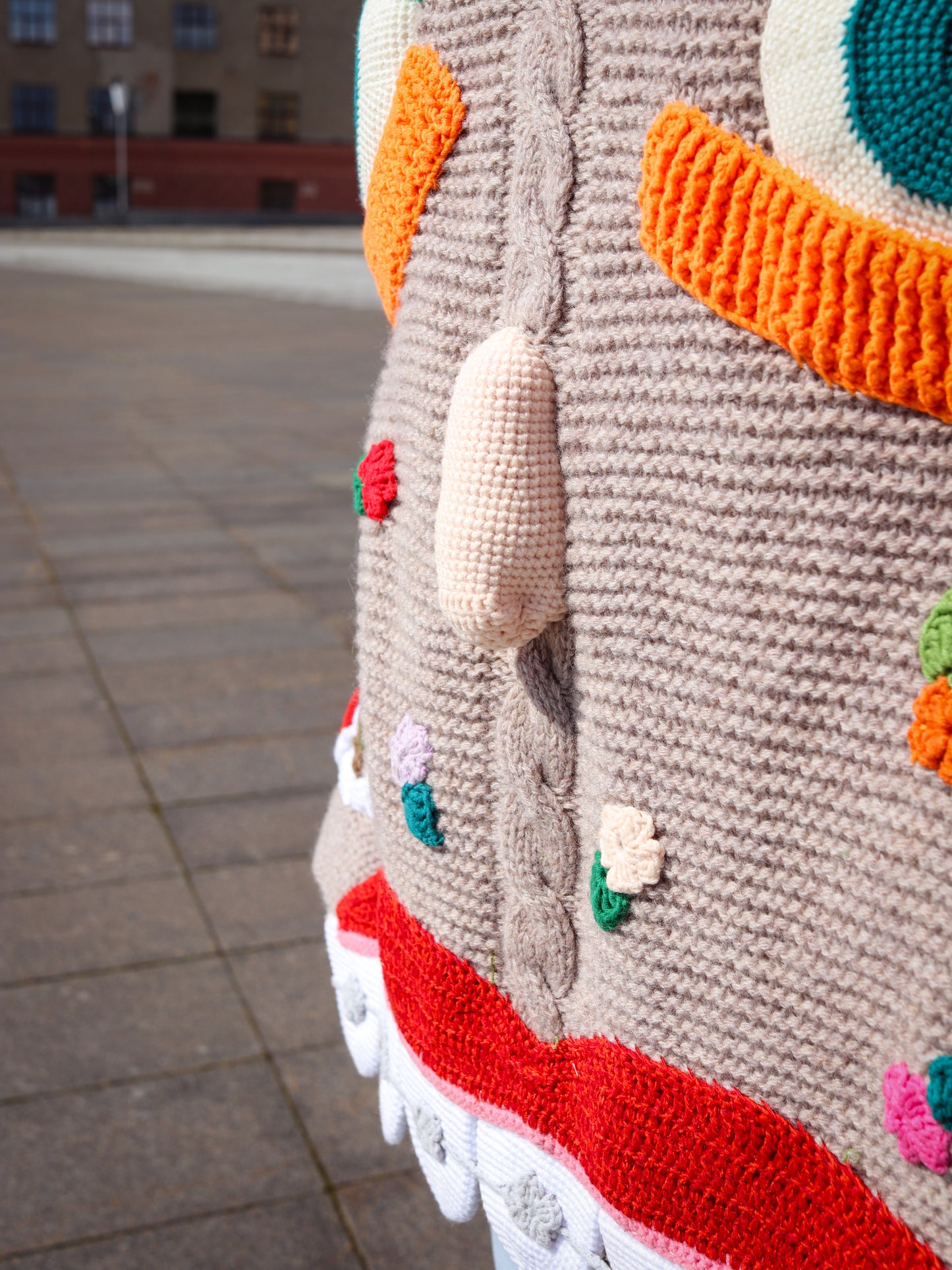 Close-up of a person wearing a colorful knitted sweater with unique design on a pavement background