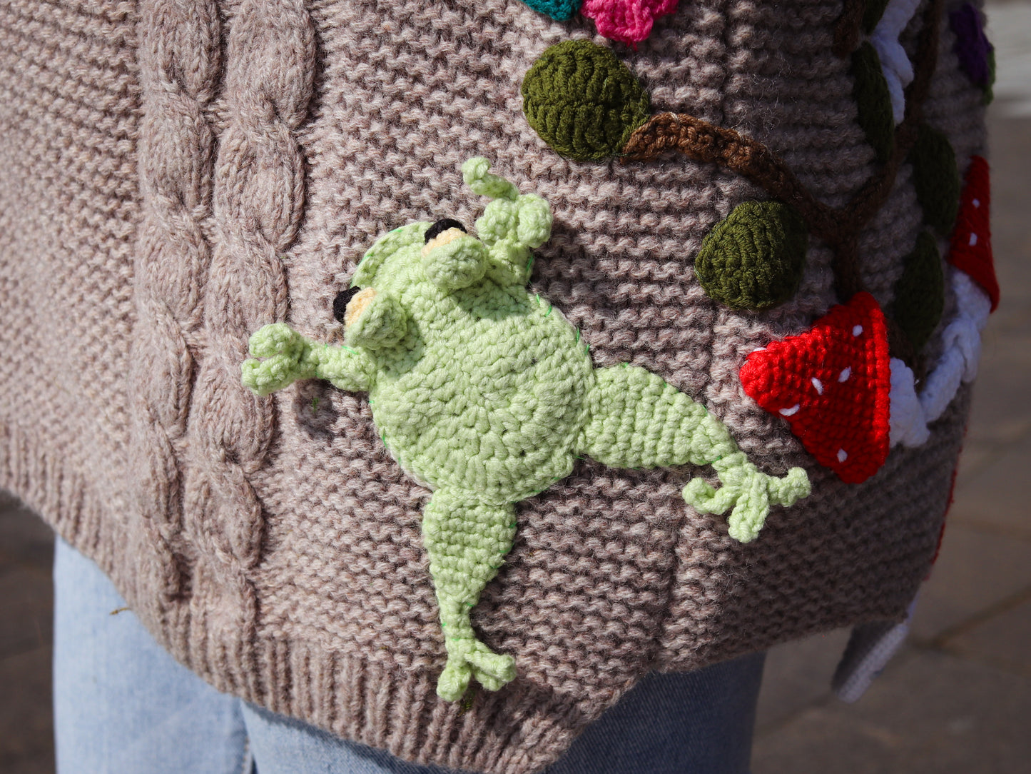 Brown knitted sweater with a green frog patch and colorful elements.