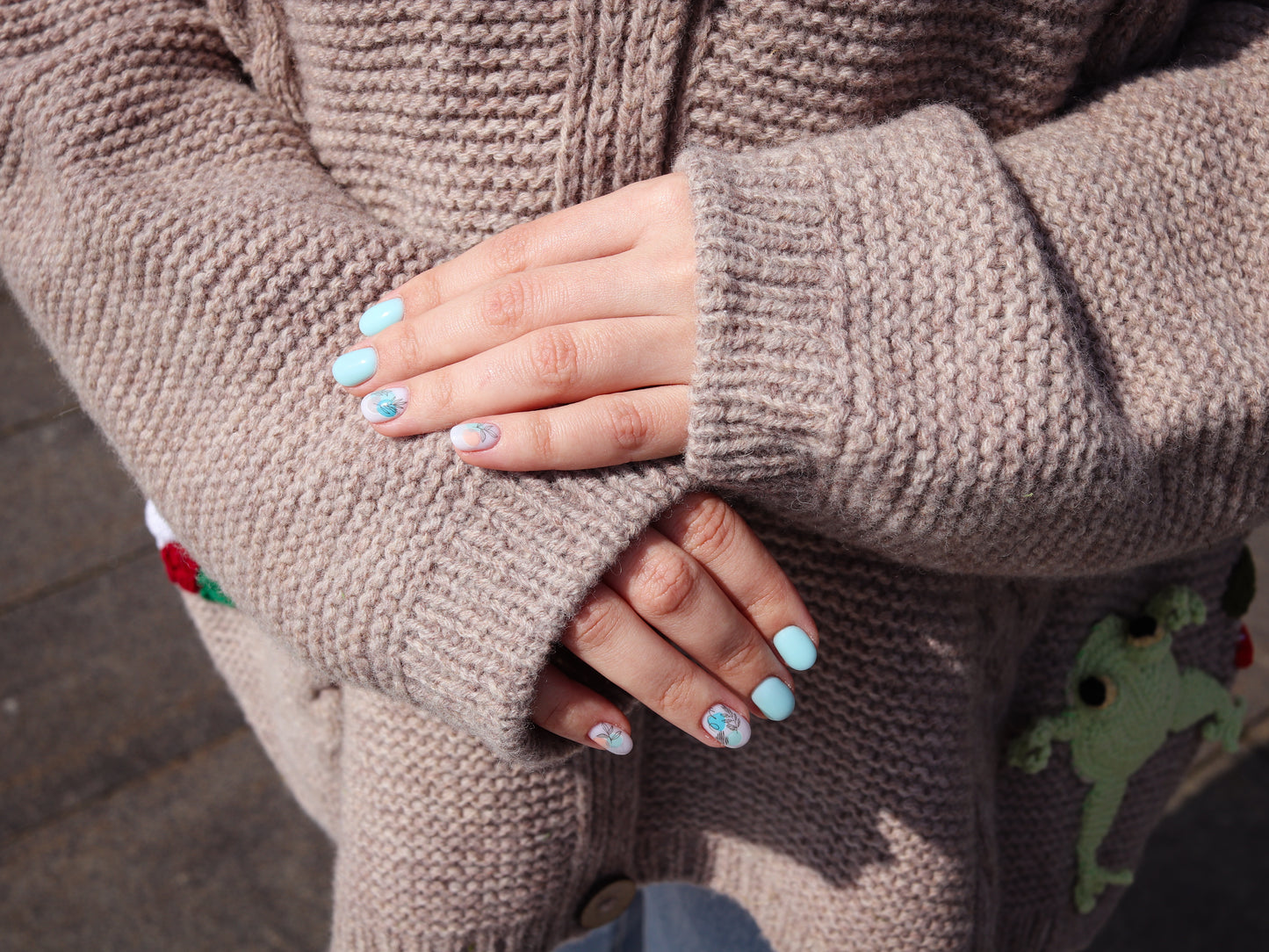 Close-up of hands wearing a beige knitted sweater with colorful buttons.