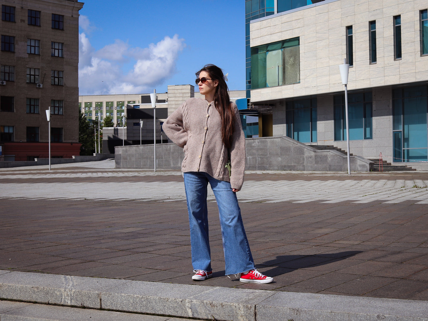Woman in cardigan standing on a sidewalk with buildings in the background