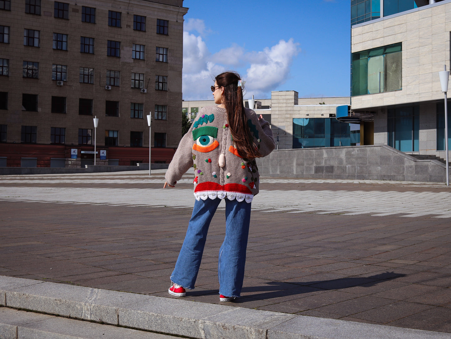 Person wearing a colorful sweater with a unique design, standing on a city street.