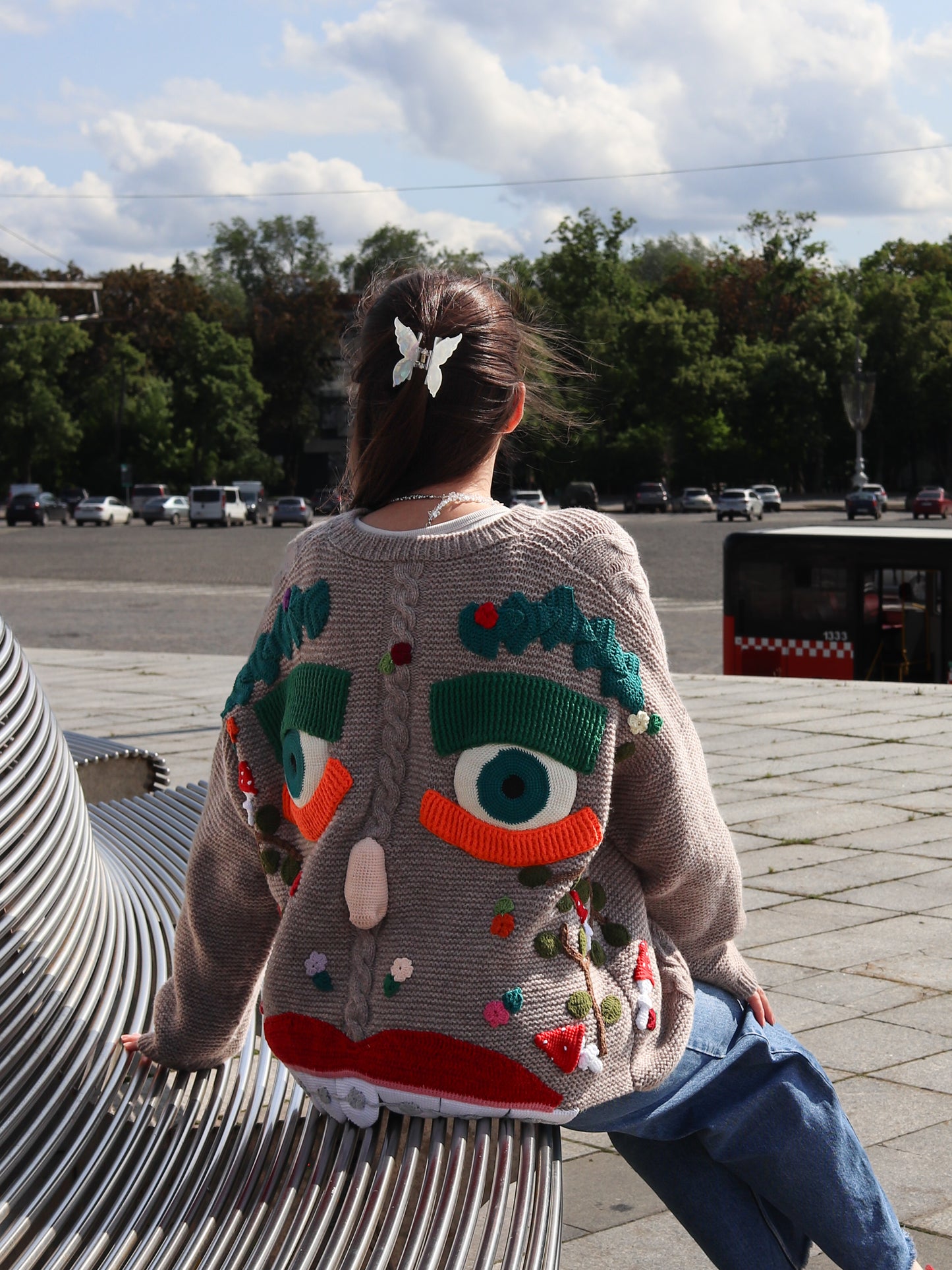 Person wearing a colorful, patterned sweater sitting on a bench outdoors.