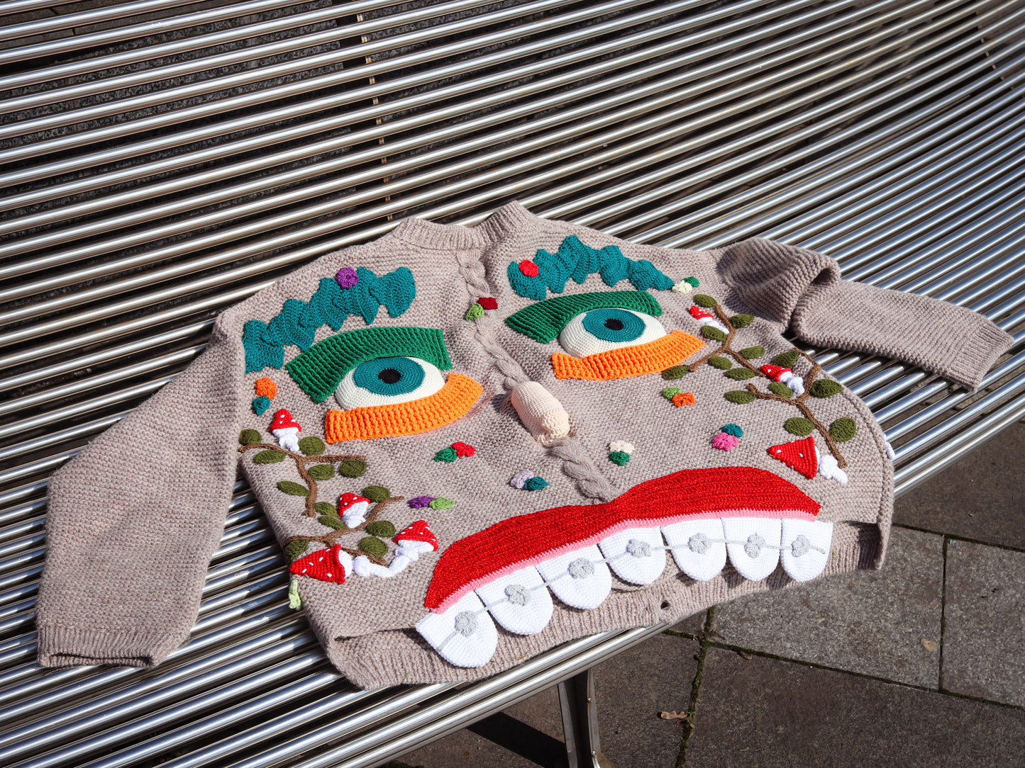 Unique knit sweater with colorful monster face design on a metal surface