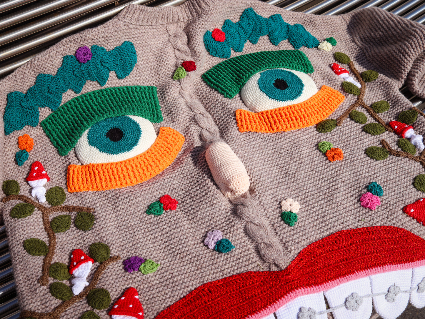 Knitted sweater with colorful eye design and small figures on a textured surface