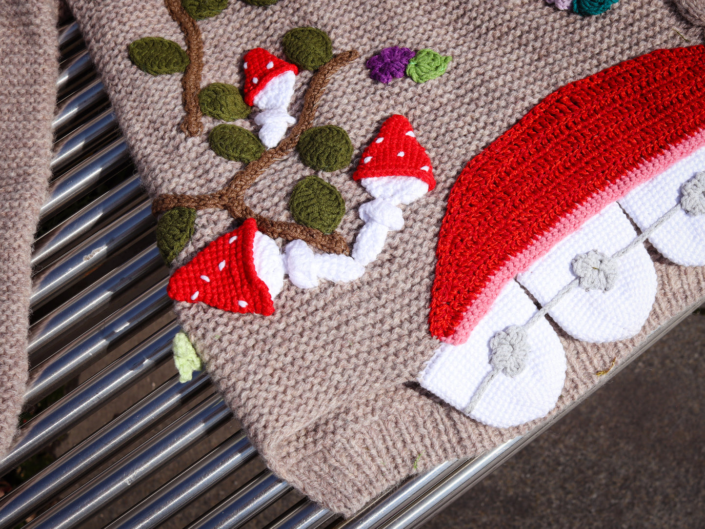 Close-up of a knitted or crocheted fabric with red and white mushroom patterns on a textured surface.