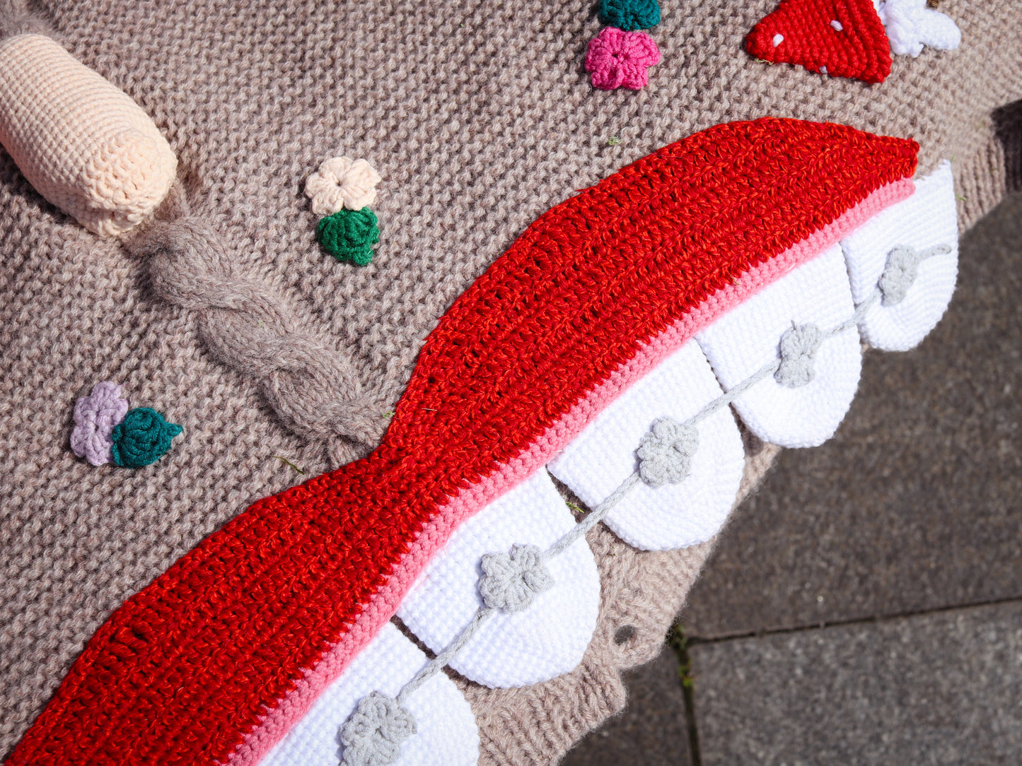 Crocheted red, white, and gray elements with floral design on a textured surface.