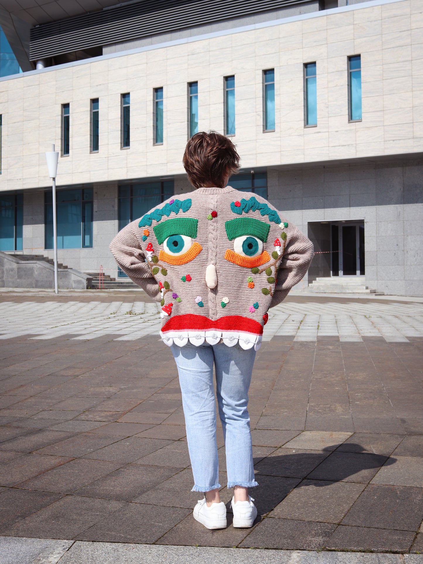 Person wearing a colorful sweater with a face design outdoors.