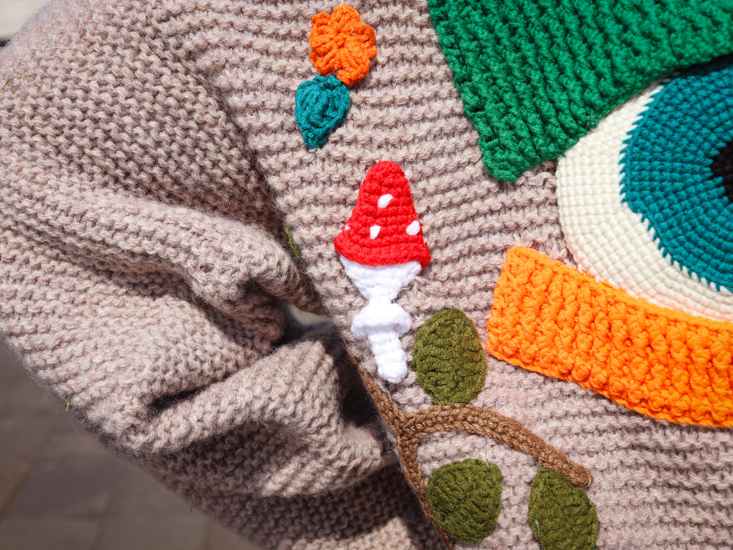 Close-up of a knitted or crocheted fabric with a face and nature-themed design.