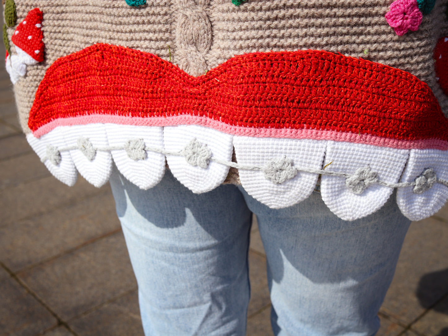 Close-up of a person wearing a red and white crocheted garment with floral details on a blurred background.