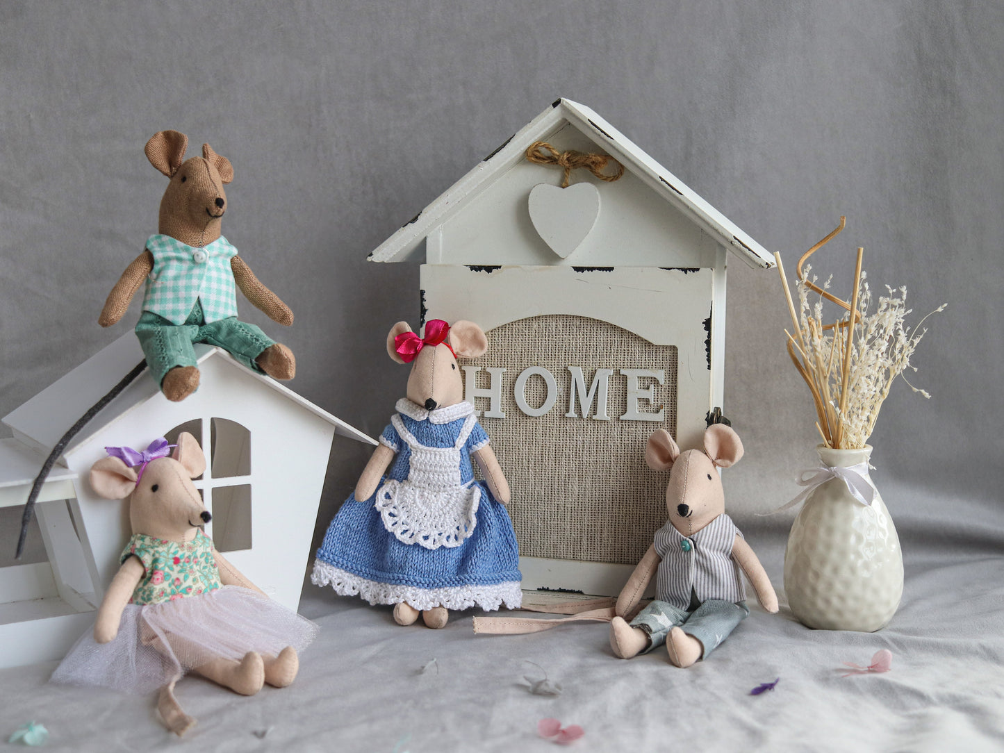 Four toy mice in front of a small house with 'HOME' written on it, on a gray surface.