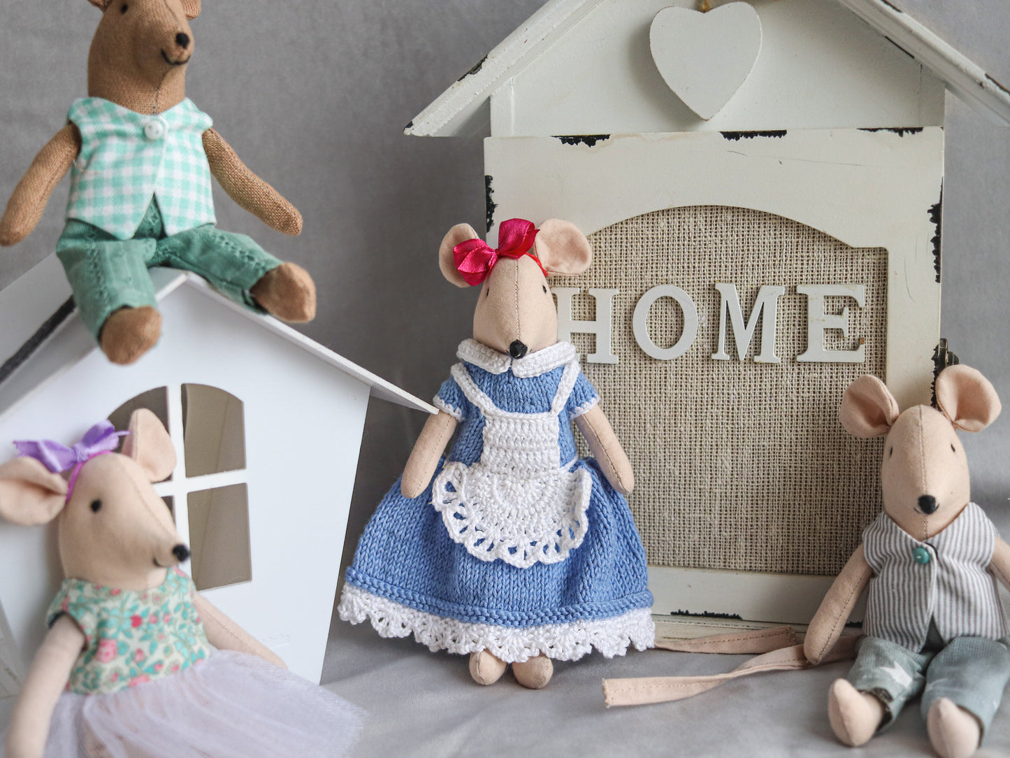 Four toy mice in dresses and outfits with a 'HOME' sign in the background.