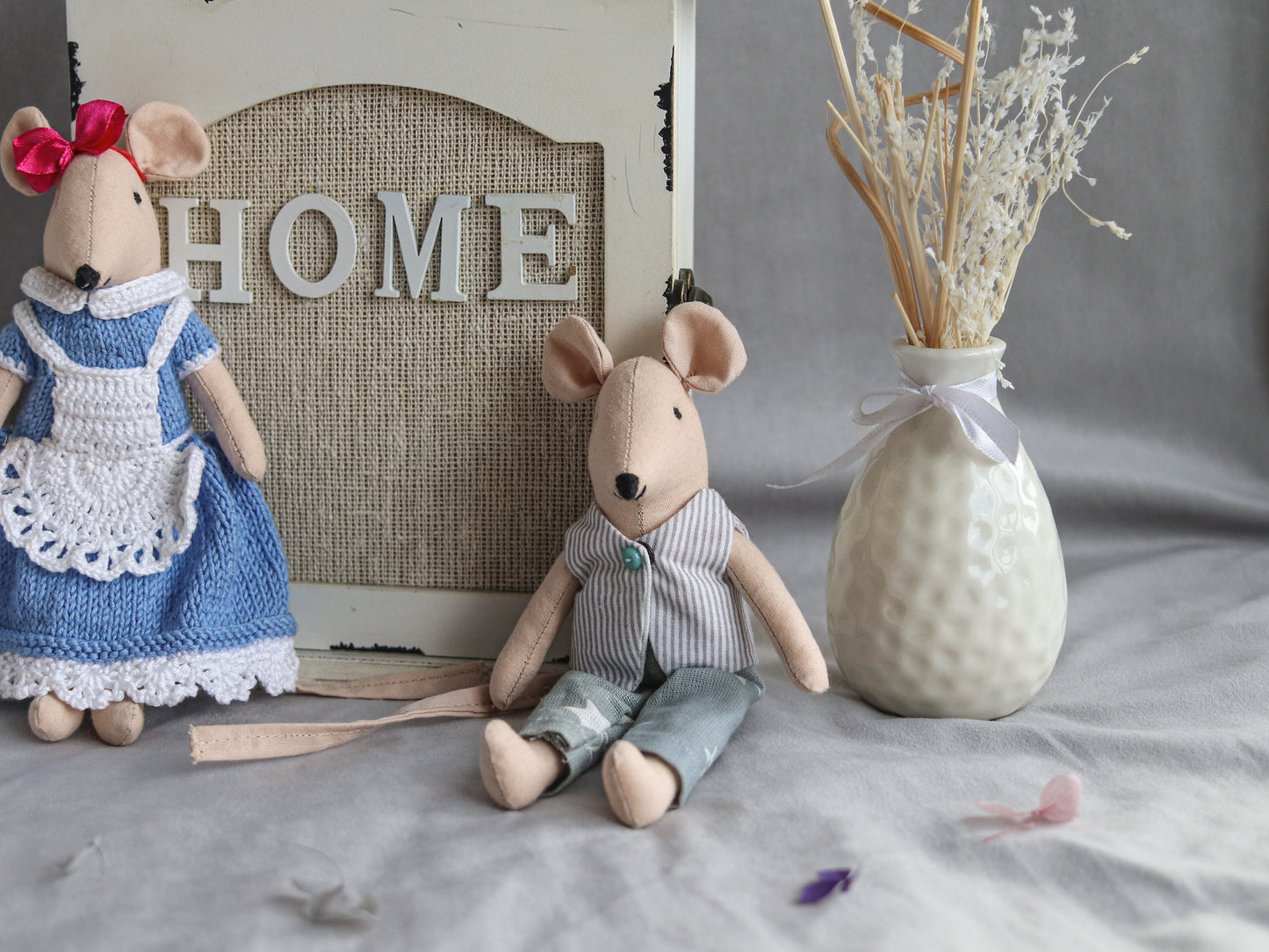 Two stuffed mouse toys and a decorative vase on a surface with 'HOME' sign in the background.