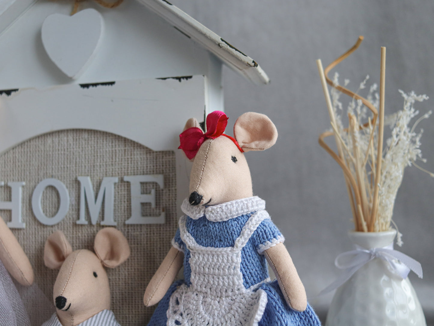 Two plush mouse toys, one in a blue dress with a red bow, the other in a white outfit, against a 'HOME' sign.