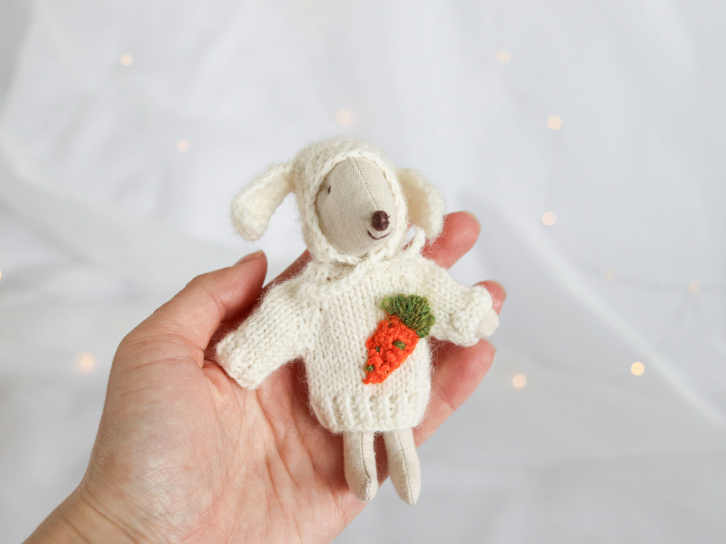 Hand holding a small Maileg Mouse wearing a sweater with a carrot on a light background