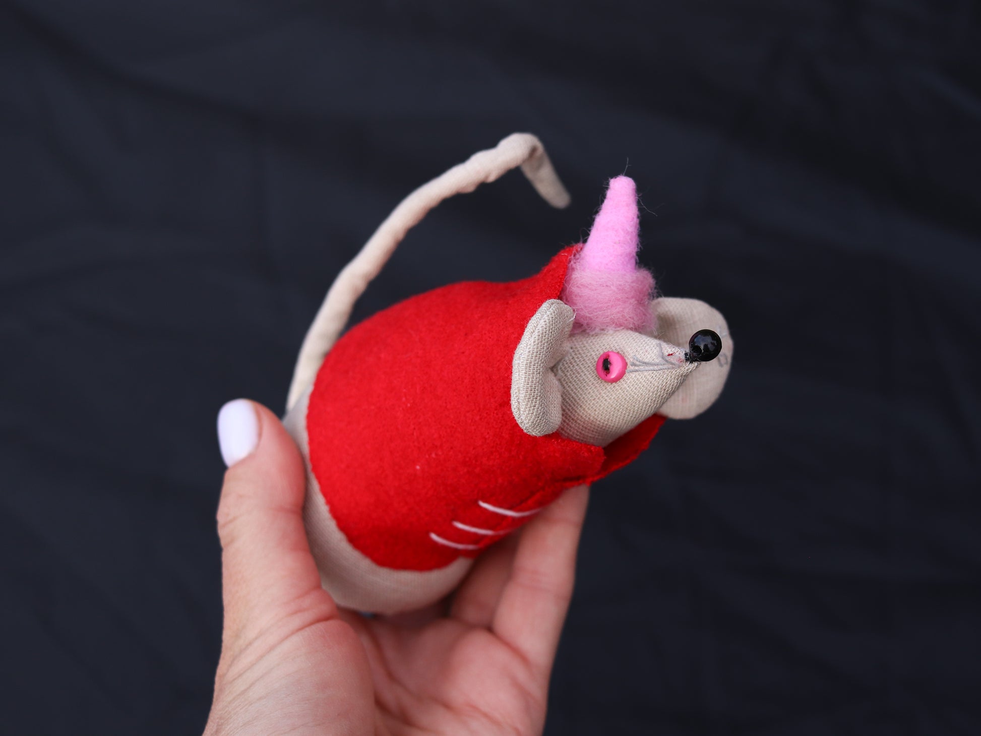 Hand holding a red mouse toy with a pink element against a dark background