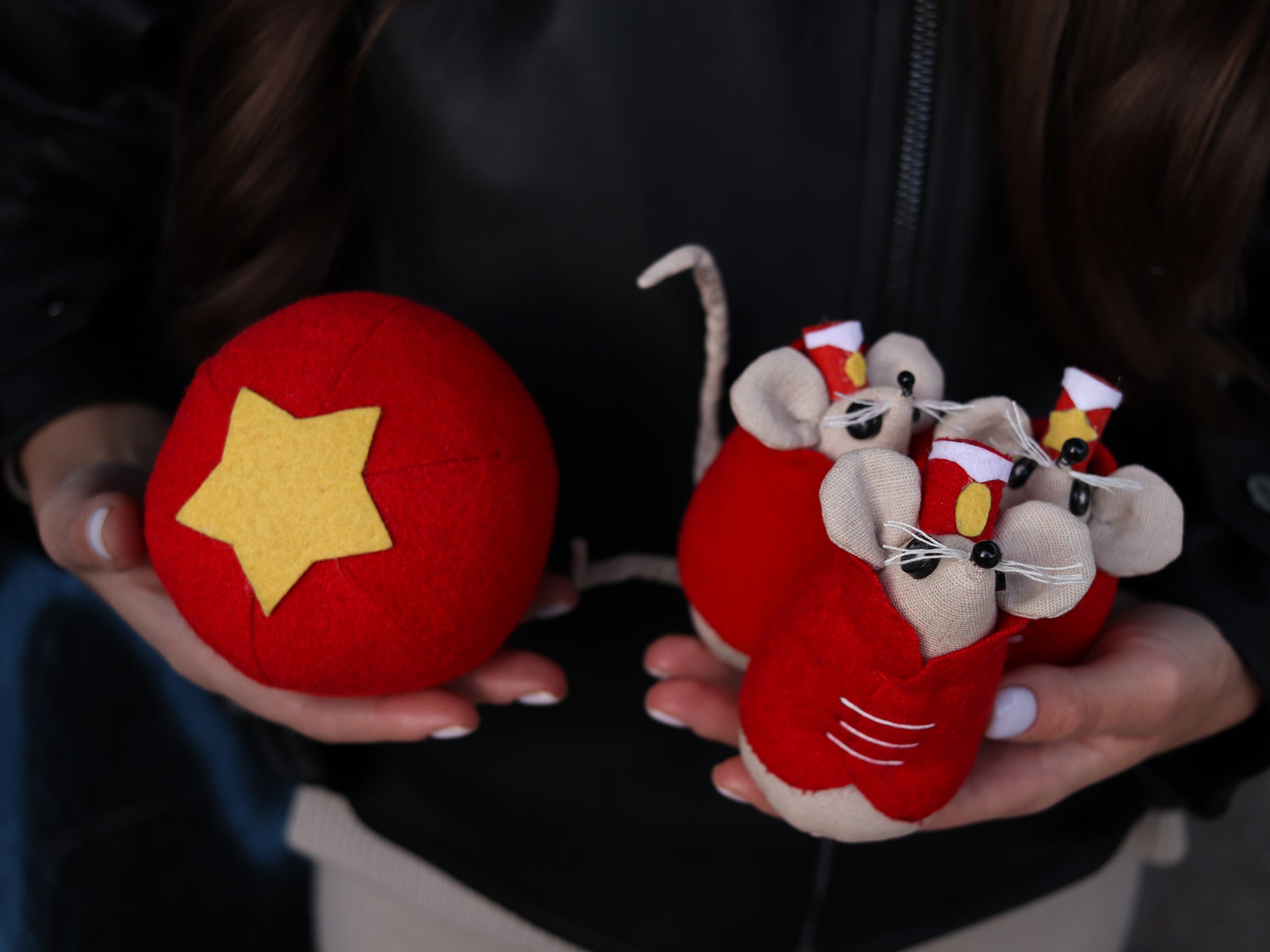 Red ball with yellow star and red plush mice held in hands against a dark background