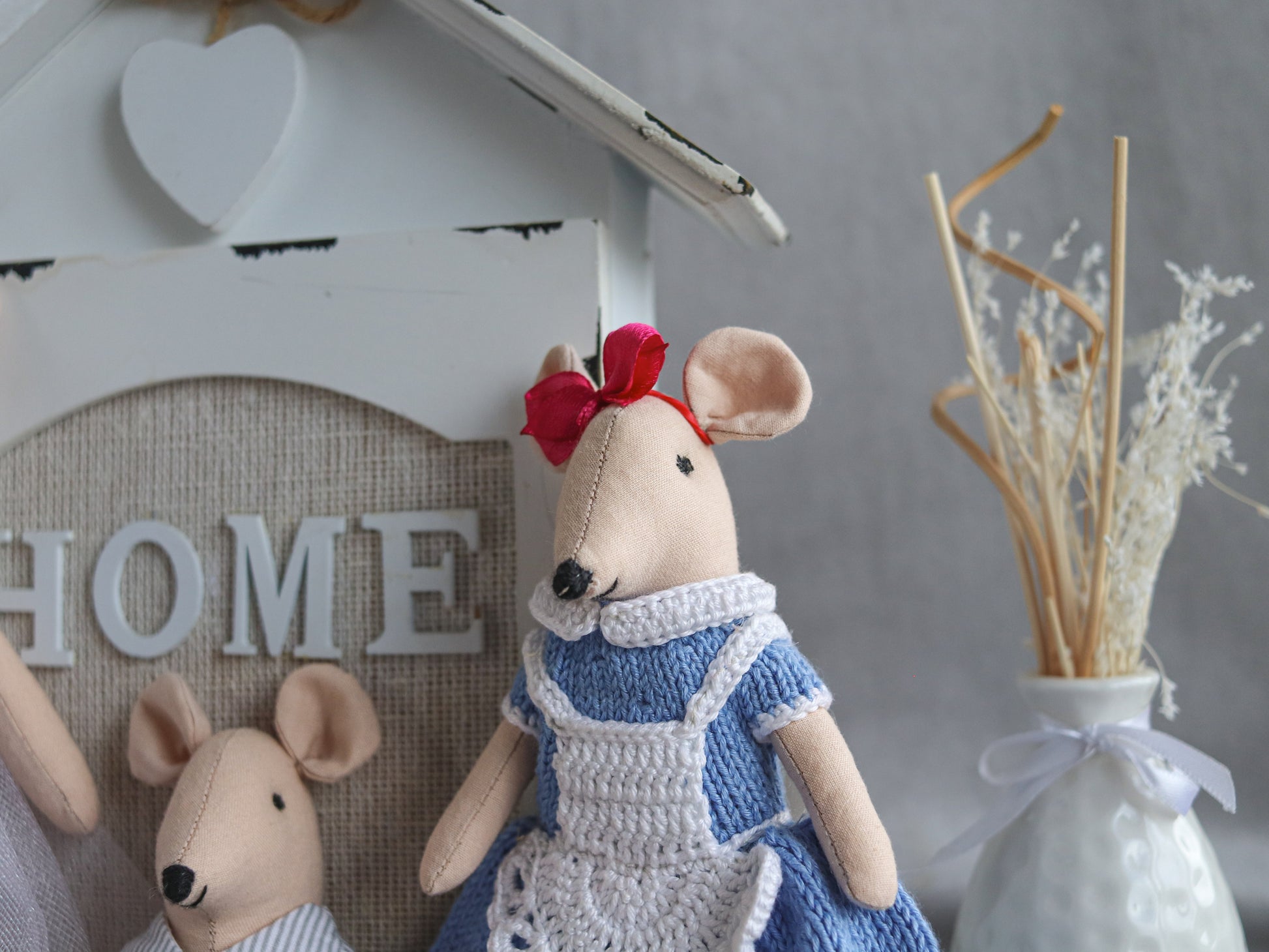 Two plush mouse toys, one in a blue dress with a red bow, the other in a white outfit, against a 'HOME' sign.